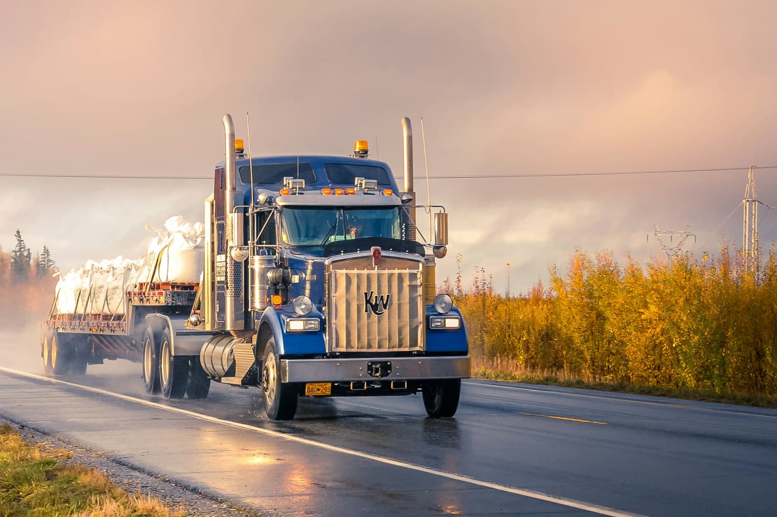 Blue semi-truck on a wet highway at golden hour